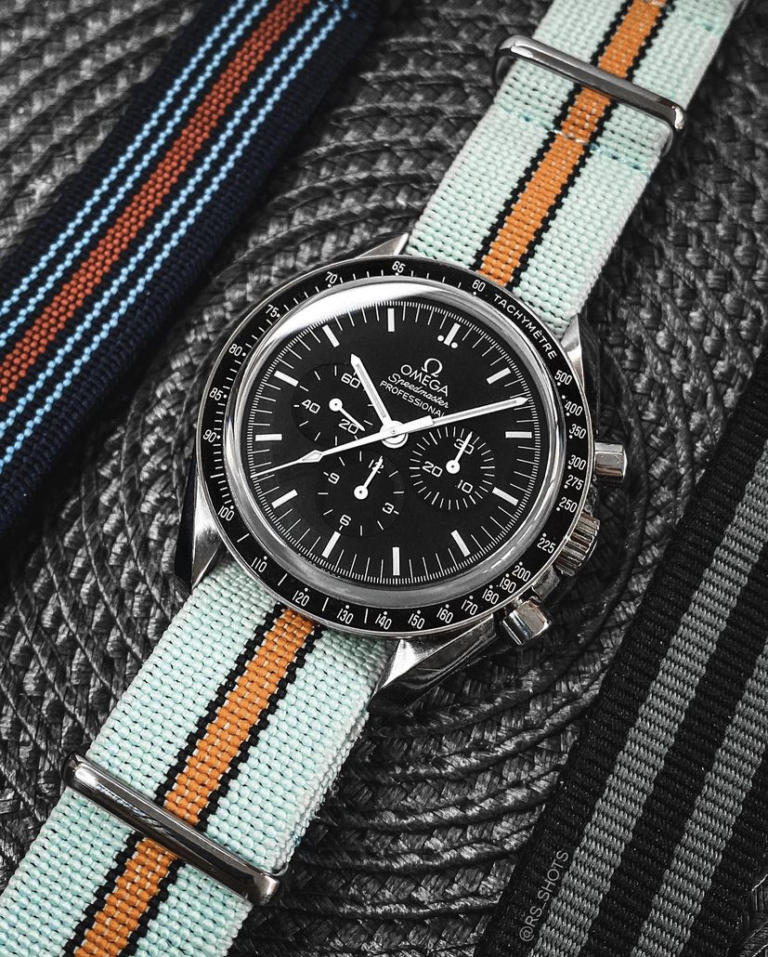 Omega Speedmaster wristwatch photographed on a striped fabric strap.